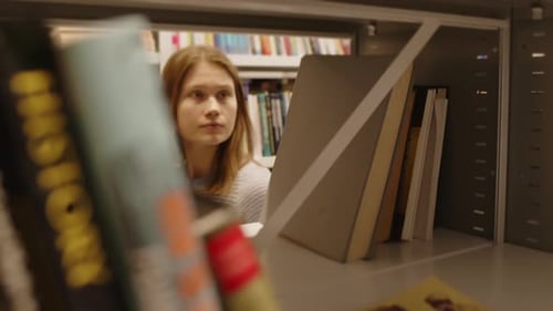 Female Student Taking Book from Shelf in College Library