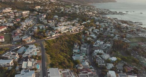 Drone flies slowly over Camps Bay beach in Cape Town South Africa - many houses on the hillside and
