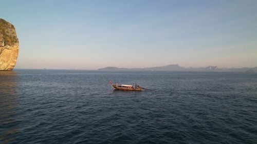 aerial drone approaching a thail longtail boat anchored in the water of Krabi Thailand during a sunr