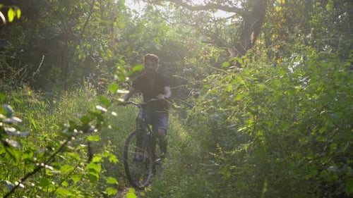 boy man cycling in deep jungle front camera sunlight rays flairs in-camera cinematic off-road cycli