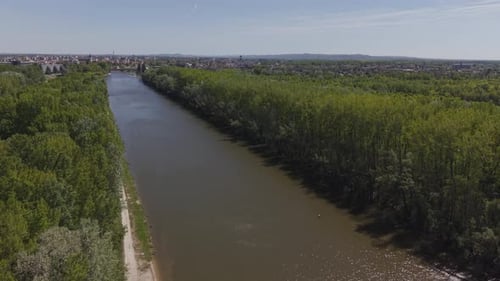 Aerial view of a calm river flowing through dense green forest with a distant cityscape on the
