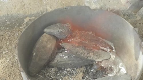 Molten lead in a metal container, glistening with heat from torch, close up