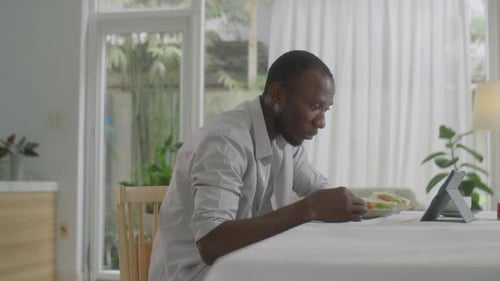 Man Eating Lunch and Looking at Tablet