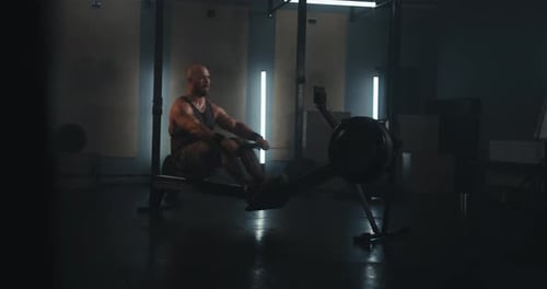 Athletic Bearded Man in a Tank Top Exercising on a Rowing Machine in a Contemporary Gym Setting