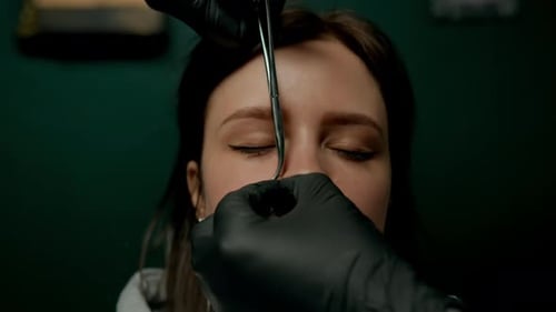 Interior de un estudio de piercings: el maestro de piercings hace un piercing para una niña, piercing para el tabique nasal