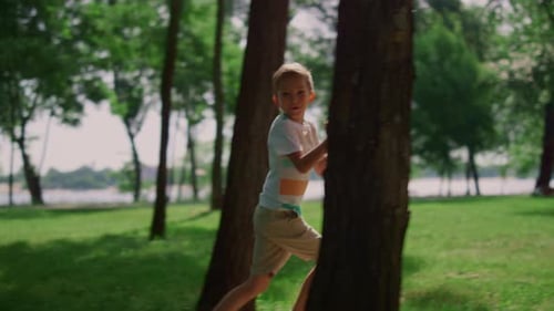 Happy smiling boy running in green park on sunny summer day enjoying joyful nature