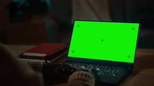 Beautiful Black Woman Sitting at Her Desk Works on a Laptop with Green Chroma Key Screen. Late at N