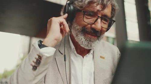 Clouse up, mature businessman and headphones, sits in an outdoor cafe and works using tablet