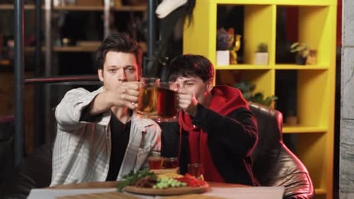 Dos jóvenes alegres están bebiendo cerveza sentados en una mesa en el bar