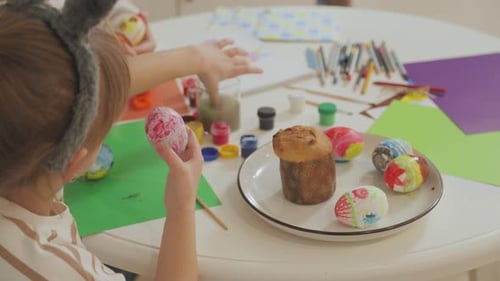 Young beautiful mother and charming daughter are painting Easter eggs.