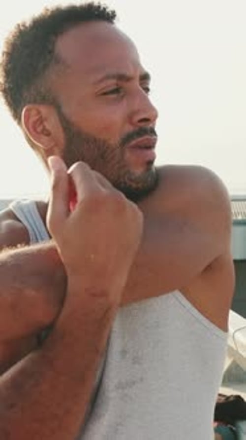 Young athlete doing warm-up, stretching his arms before training while standing on the embankment
