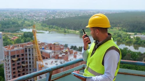 Männlicher Ingenieur trägt eine Sicherheitsweste mit Helm und hält Walkie-Talkie in der Hand, während er die Wohnsiedlung von