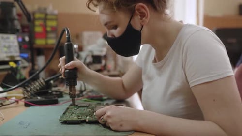 Female Electronic Repair Service Center Worker Repairs Electronic Boards and Soldering Microchip