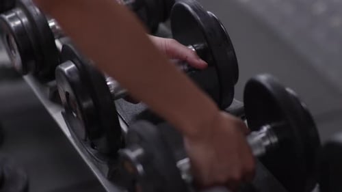 Footage of Close up hands picking up dumbbell weights on racks.