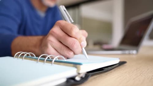 Person Writing in Notebook at Desk with Laptop