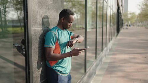 Man Using Phone and Checking Watch Outdoors