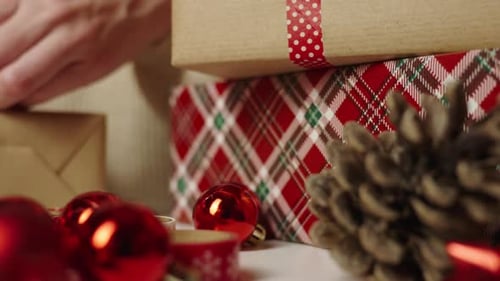 Hands Wrapping Christmas Gift with Ribbon and Ornaments