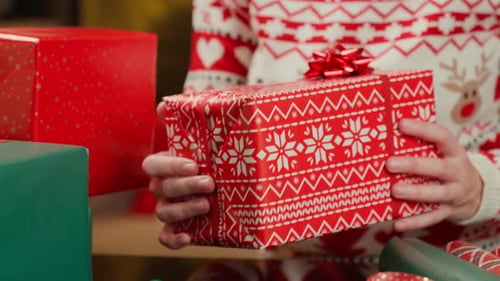 Woman holding wrapped Christmas gift on table with wrapping paper and ribbon
