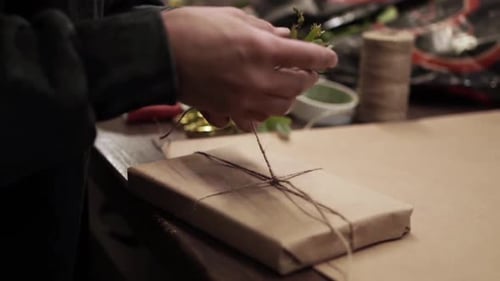 Hands Decorating Wrapped Gift with Greenery