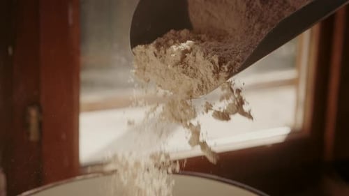 Close-up of fresh white flour in a measuring scoop. Slow-motion falling flour.