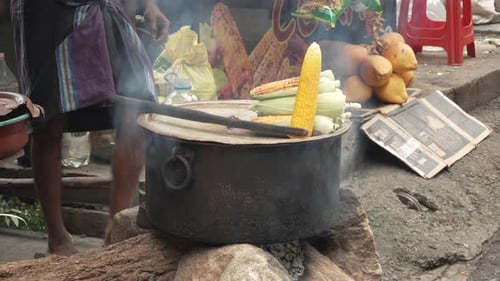Street Vendor Boiling Corn Cobs in Large Pot Over Wood Fire with Steam Sri Lanka