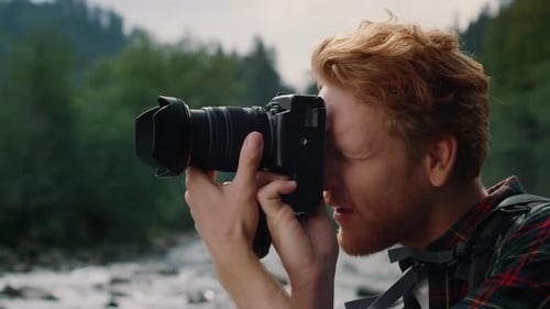 Closeup View Of Photographer Using Photo Camera Outdoor. Redhead Man Taking Photos On Professiona...