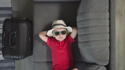 Boy with Hat and Suitcase Relaxing on Couch