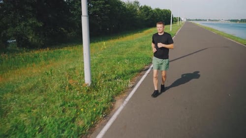 Young Caucasian Man Running Along the Embankment in the Morning Daylight A Jogging Track Along the