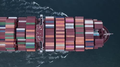 Aerial top view of a loaded container cargo vessel traveling over ocean.