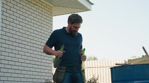 Man Puts Gardening Tools in Belt By House