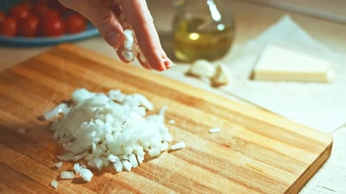 Hand Sprinkles Chopped Onions onto Cutting Board