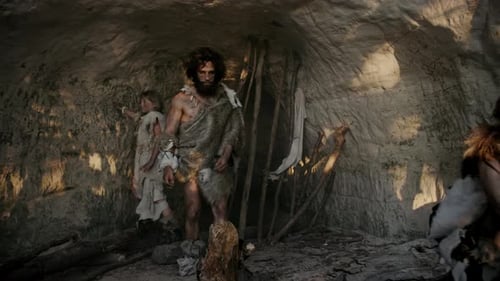 Une tribu de chasseurs-cueilleurs en peau d'animal vit dans une grotte. Le leader tient un outil à pointe de pierre et
va