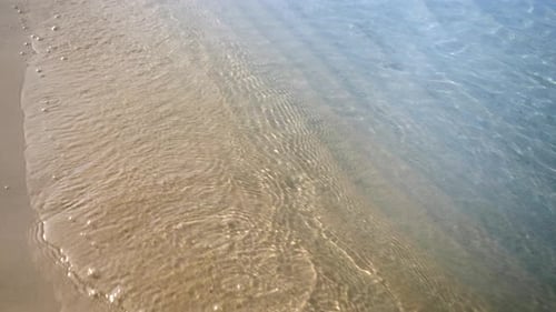Zeitlupe einer Kamera, die über ruhige Meereswellen fliegt, die am Sandstrand rollen.