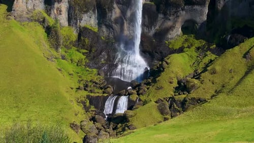 Aerial view of waterfall and cliff in lush valley, Iceland.