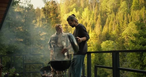 A Brunette Guy and a Blonde Girl are Watching the Preparation of Meat on the Grill During a Picnic
