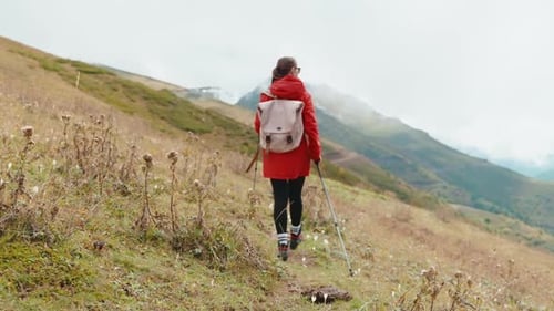 Back View of Girl Hiking in Mountain Walking Along Slope on Path Holding Sticks