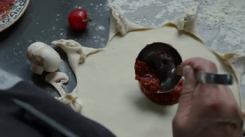 Chef preparing pizza in the restaurant kitchen. The tomato sauce is putting on the pizza dough.