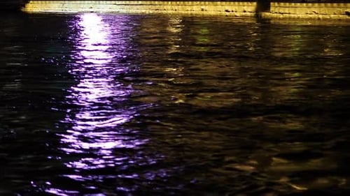 Lights reflect on water surface in night. River stream.