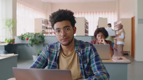 Porträt eines Biracial Guy mit Laptop, der in der Bibliothek studiert