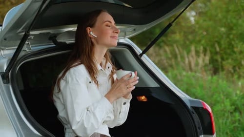 The Woman in the Car A Smiling Beautiful Girl Listens to Music with Headphones Drinks Tea Sitting on