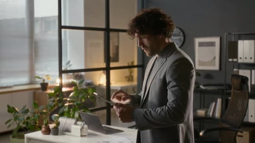 Curly-Haired Male Manager Using Internet on Digital Tablet Working in Office