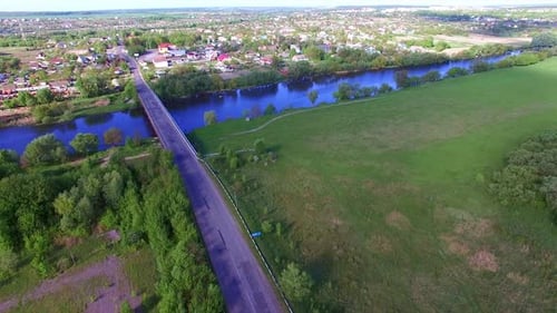 Blue river separating the village from farmlands. Little concrete bridge over the river.