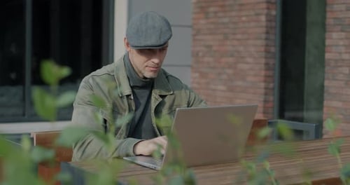 Young Man Freelancer Working with Laptop Sitting in Outdoor Cafe Concentrated on Business Activity