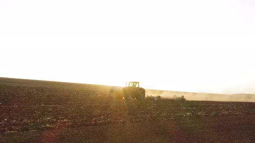 Red Tractor plowing a large field, Early morning follow footage with mild flare.