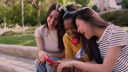 Friends Laughing Together at Smartphone in the Park