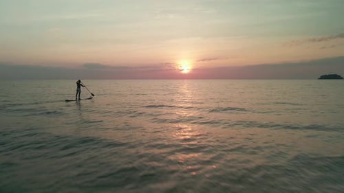 Drone flying towards a man paddle boarding in the ocean at golden hour