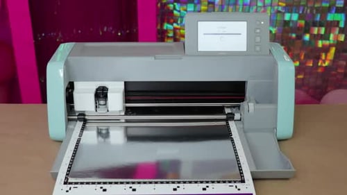 A plotter cutting silver metallic cardboard on colorful background, close-up