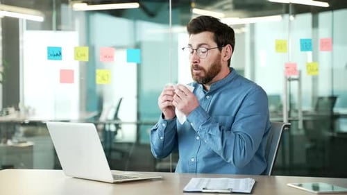 Man Sneezing at Desk Working on Laptop