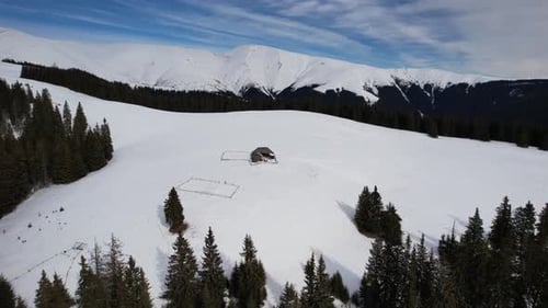 Aerial drone view of a snow-covered cabin in a peaceful mountain landscape in winter