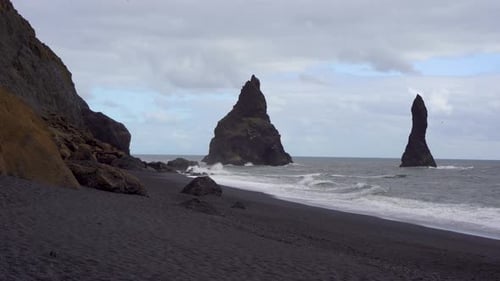 Black sand beach with towering sea stacks under a cloudy sky in Iceland, dramatic coastal landscape